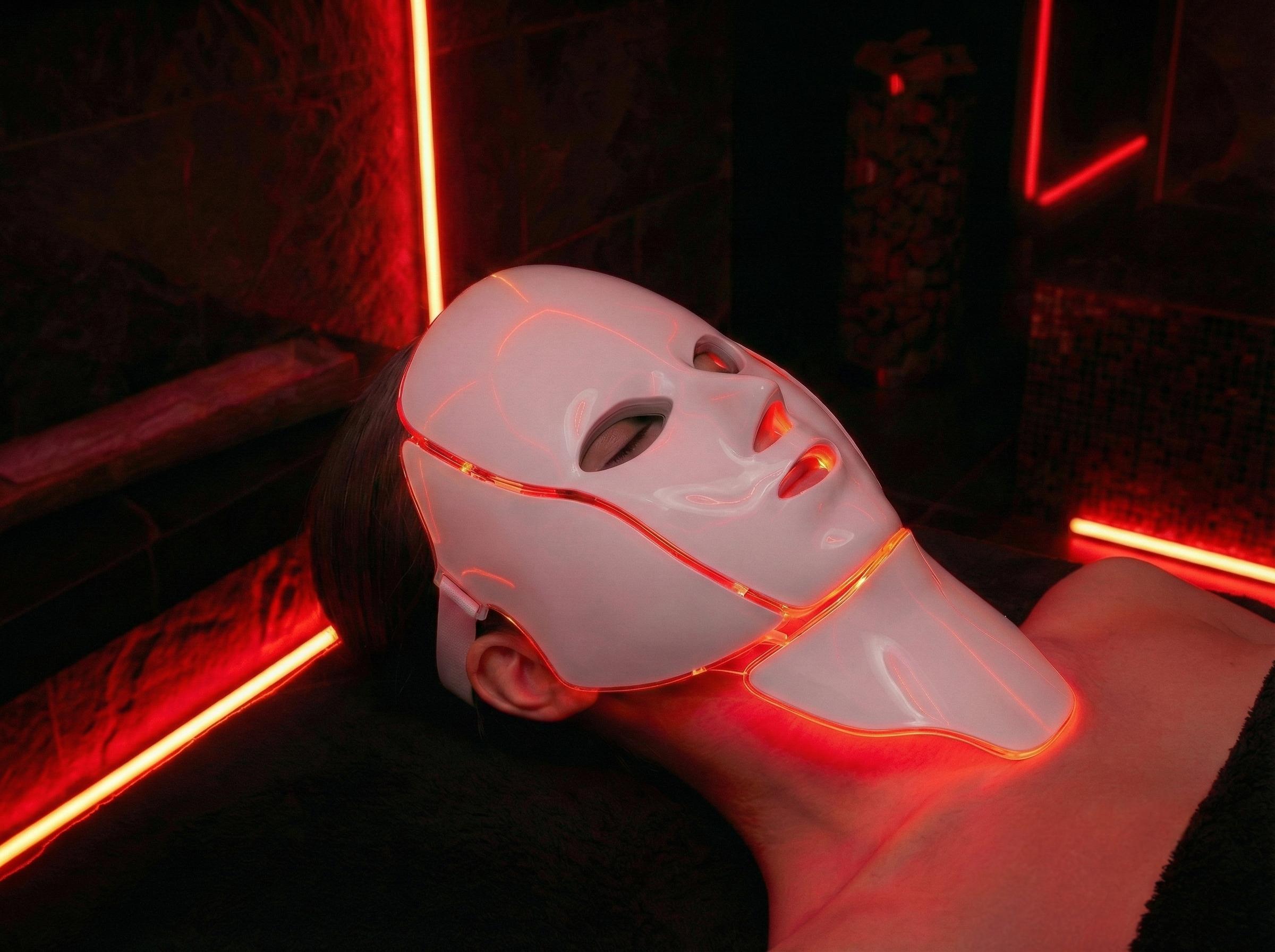 Person wearing LuceRosso red light therapy mask in dark spa setting for LED skin treatment