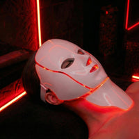 Person wearing LuceRosso red light therapy mask in dark spa setting for LED skin treatment
